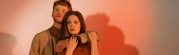 Redhead young man hugging pretty girlfriend on red background, banner — Stock Photo