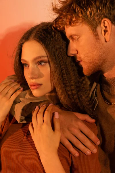 Portrait of young man with closed eyes hugging pretty girlfriend on red — Photo de stock