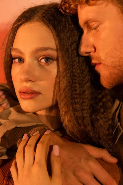 Portrait of young man with closed eyes hugging pretty girlfriend looking at camera on red — Photo de stock