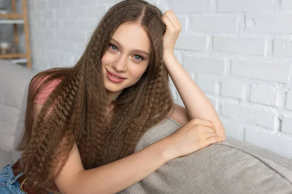 Joyful teenage girl in casual clothes sitting on couch in modern living room — Fotografia de Stock