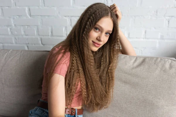 Pleased teenage girl in casual clothes sitting on couch in modern living room — Fotografia de Stock