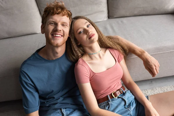 High angle view of young couple smiling while sitting near couch in modern living room — Fotografia de Stock