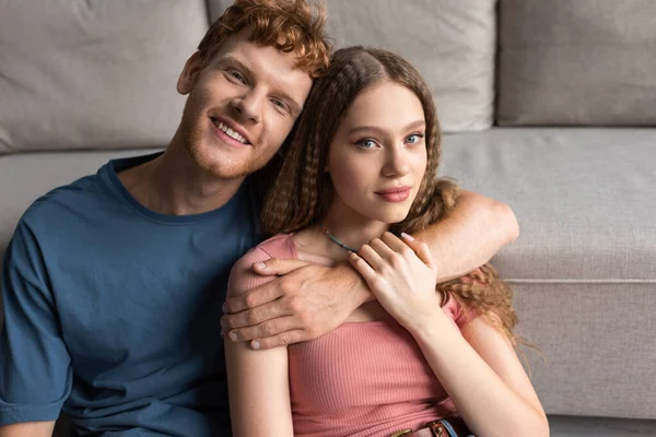 Redhead young man smiling and hugging pretty girlfriend in living room — Fotografia de Stock