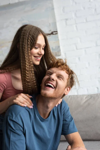 Cheerful teen girl smiling and hugging excited boyfriend in living room — Foto stock