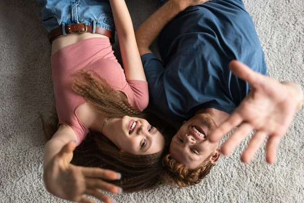 Вид зверху щасливий і молодий чоловік і весела дівчина жестикулює, лежачи на килимі — стокове фото