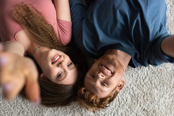 Top view of happy and young man and cheerful girlfriend smiling while lying on carpet — Fotografia de Stock