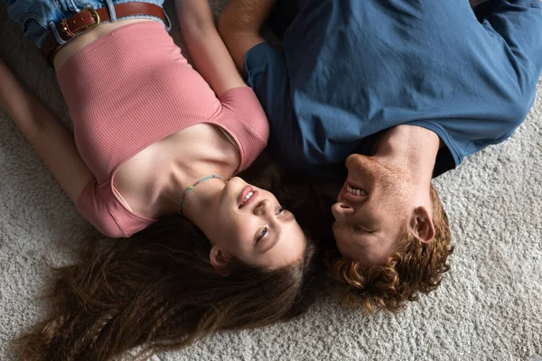 Top view of happy young couple smiling and lying together on carpet in living room — Stock Photo