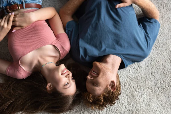 Top view of cheerful young couple smiling and lying together on carpet in living room - foto de stock