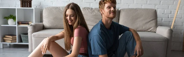 Happy young couple sitting next to each other in modern living room, banner — Foto stock