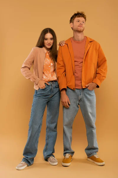 Full length of happy young couple in autumnal outfits and gumshoes posing together on beige — Photo de stock