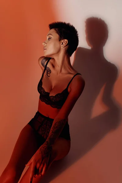Hochwinkel-Ansicht von sexy Frau in schwarzen Dessous auf blassrotem Hintergrund mit Schatten — Stockfoto