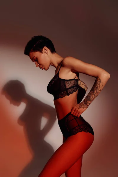 Side view of sexy brunette woman touching lace panties on brown and red background with shadow — Stock Photo