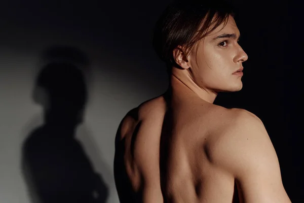 Joven hombre sin camisa mirando hacia otro lado sobre fondo negro y gris - foto de stock