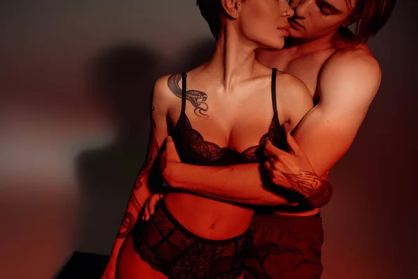 Partial view of tattooed woman in black lingerie near shirtless man on burgundy background — Stock Photo