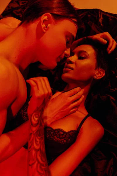 Vista dall'alto della donna tatuata e del giovane che fa l'amore su biancheria da letto di seta nera a luce rossa — Foto stock
