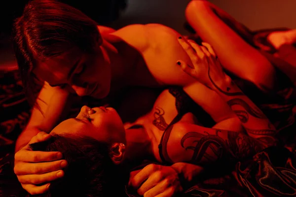 Giovane coppia appassionata fare l'amore su biancheria da letto in raso nero a luce rossa — Foto stock