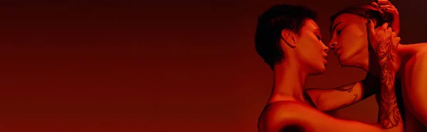 Vue latérale de jeune femme tatouée embrassant et embrassant homme torse nu isolé sur rouge, bannière — Photo de stock