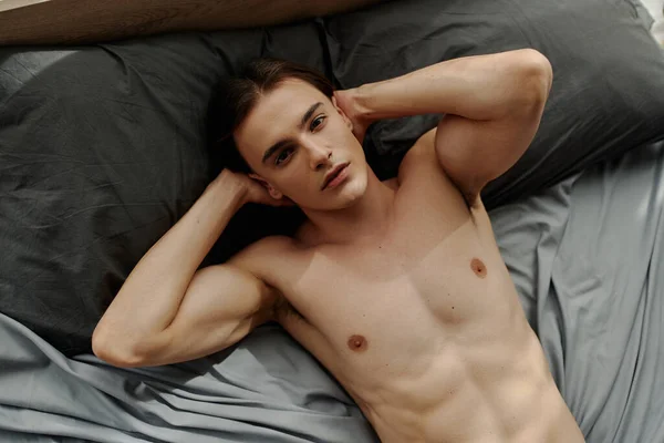 Вид сверху молодого и сексуального мужчины, лежащего дома на кровати и смотрящего в камеру — стоковое фото
