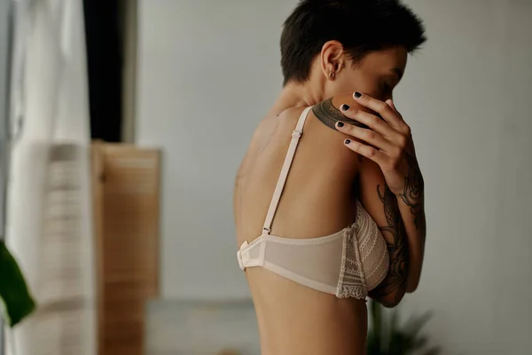 Side view of brunette woman in beige bra embracing herself in bedroom — Stock Photo