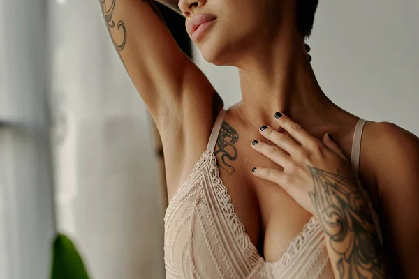 Vista ritagliata della donna tatuata in reggiseno di pizzo toccare petto a casa — Foto stock