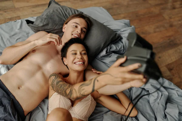 Vista superior de pareja sexy tomando selfie en la cámara vintage en la cama - foto de stock