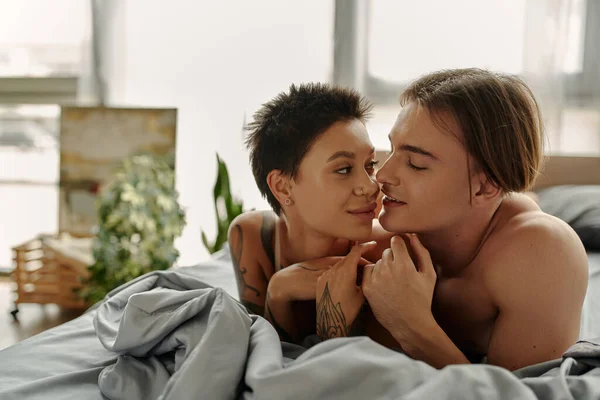 Smiling man kissing tattooed girlfriend on bed in morning — Stock Photo