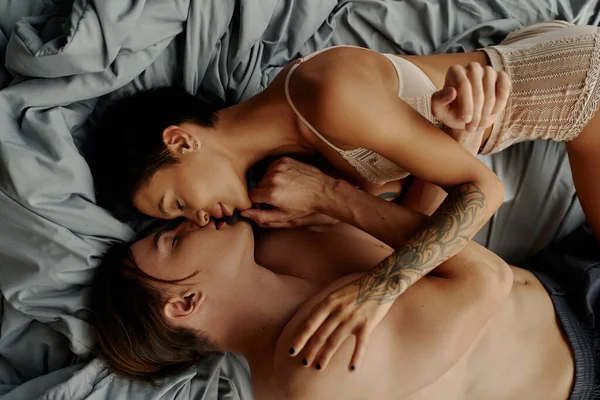 Top view of young brunette couple kissing while lying on bed — Stock Photo