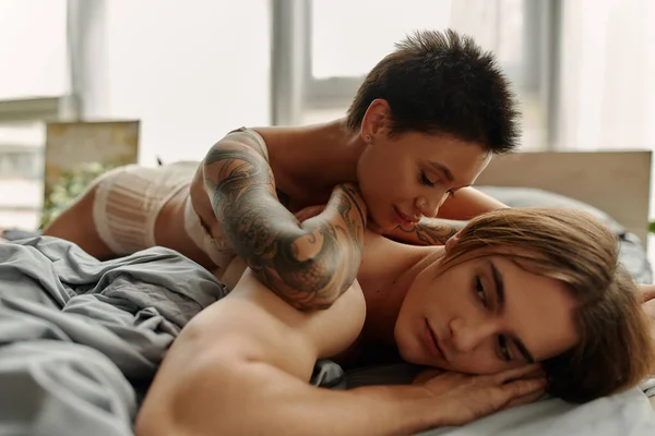 Молода татуйована жінка лежить на спині м'язового хлопця в спальні — стокове фото