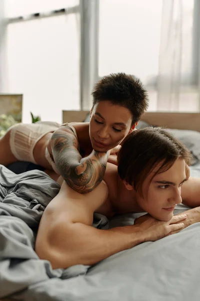 Short haired tattooed woman lying on back of boyfriend in bedroom — Stock Photo