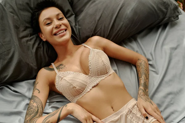Visão superior da mulher de cabelos curtos em lingerie sorrindo para a câmera na cama — Fotografia de Stock
