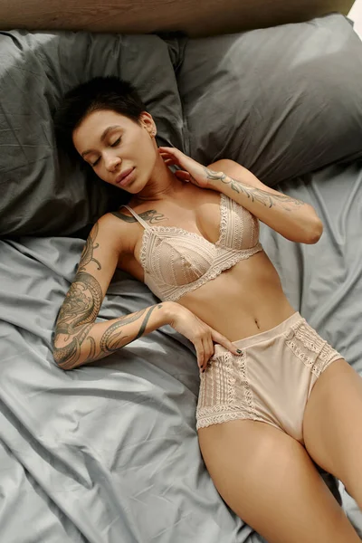 Top view of sensual woman in lace bra and panties touching neck on bed — Stock Photo