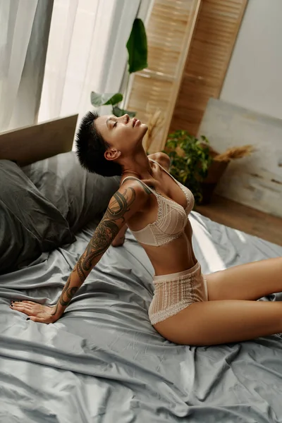 Femme sexy en sous-vêtements assis sur la literie grise le matin — Photo de stock