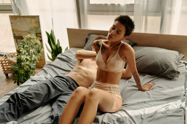 Сексуальная женщина в нижнем белье сидит на кровати рядом с размытым парнем — стоковое фото
