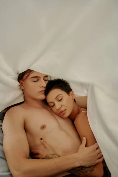Top view of muscular man hugging tattooed girlfriend under blanket at home — Stock Photo