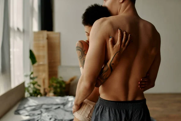 Tattooed woman in underwear hugging muscular boyfriend in bedroom — Stock Photo