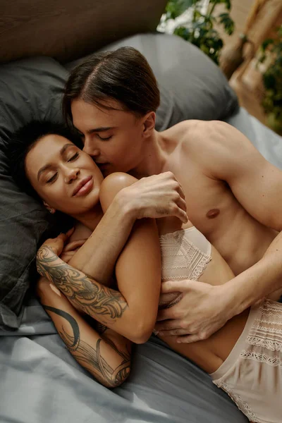 Sexy uomo baci e abbracci tatuato fidanzata sul letto — Foto stock
