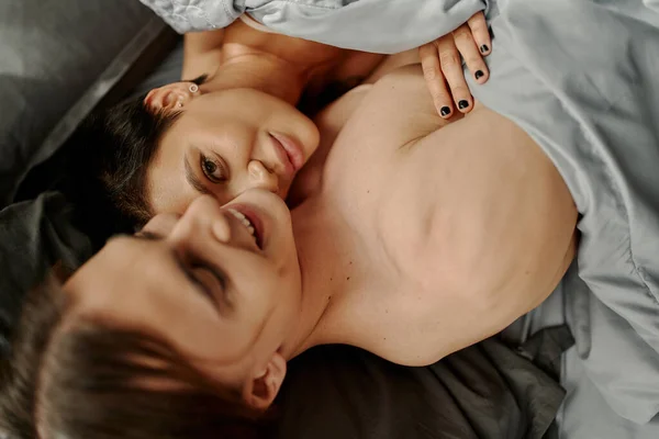 Sexy woman touching boyfriend and looking at camera on grey bedding — Stock Photo