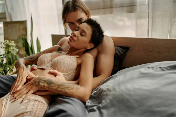 Homme torse nu regardant la caméra tout en touchant petite amie sensuelle sur le lit — Photo de stock