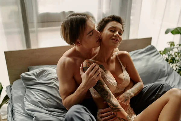 Muscular man kissing and touching tattooed girlfriend in underwear on bed in morning — Stock Photo