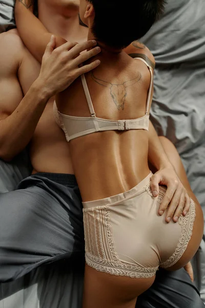 Top view of young man in pajama pants touching tattooed girlfriend in lingerie on bed — Stock Photo