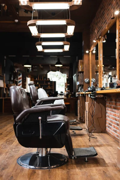 Poltronas de cabeleireiro sob lâmpadas na barbearia espaçosa — Fotografia de Stock