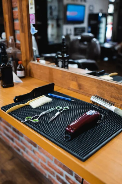Electric hair clipper and scissors near combs and blurred mirror in barbershop — Stock Photo