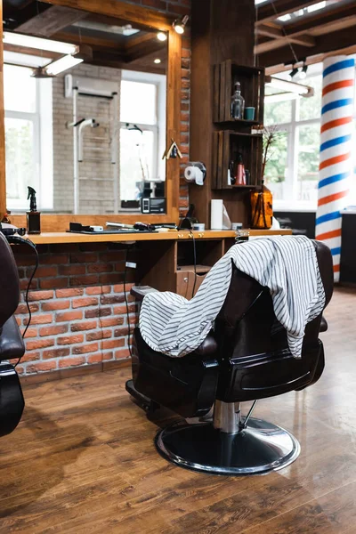 Ergonomic armchair and hairdressing cape near mirror in beauty salon — Stock Photo