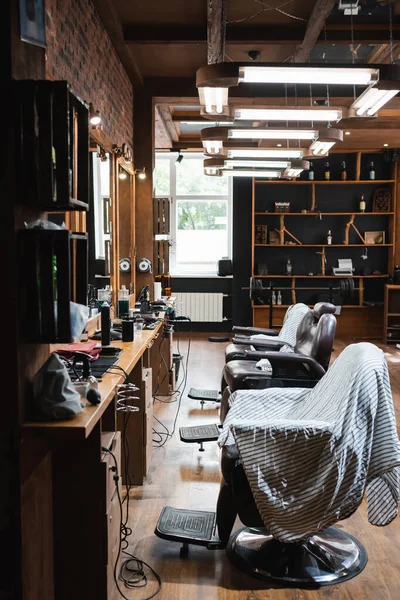 Poltronas confortáveis e capas de cabeleireiro sob lâmpadas na barbearia — Fotografia de Stock