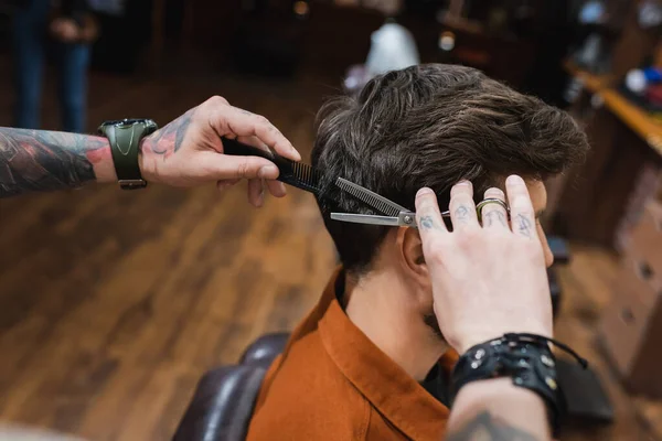 Татуйований перукар, що ріже волосся брюнетки чоловіка з тонкими ножицями — стокове фото