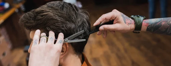 Peluquero tatuado con peine y tijeras de adelgazamiento haciendo peinado al hombre morena, pancarta - foto de stock