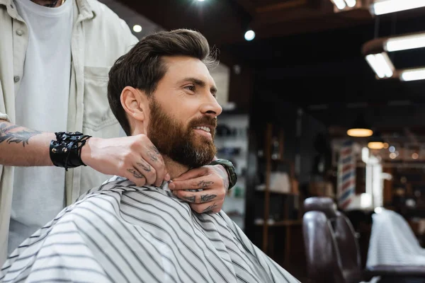 Coiffeur mettre coiffure cape sur sourire homme barbu — Photo de stock