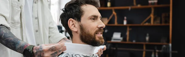 Peluquero tatuado poniendo cuello de peluquería en el cuello del cliente, bandera - foto de stock