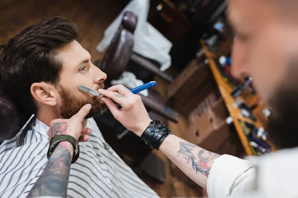 Barbiere sfocato in pelle bracciale cliente rasatura con rasoio dritto — Foto stock
