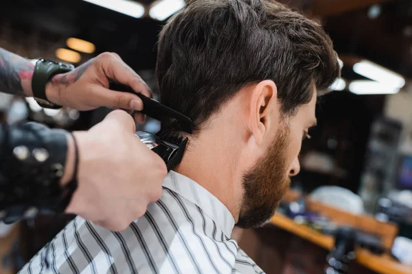 Desfocado cabeleireiro aparar morena homem com cortador de cabelo — Fotografia de Stock